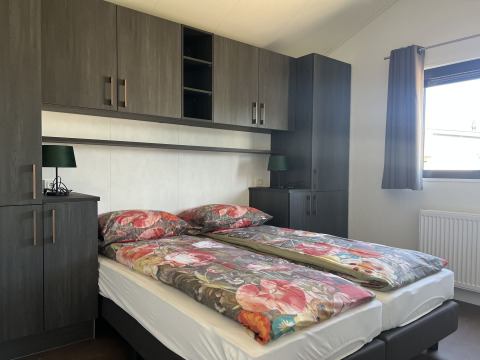 Dormitorio moderno en De Parel lodge, Vakantiepark de Zeeuwse Parel, con ropa de cama floral y armarios oscuros.