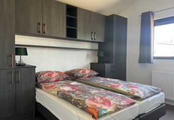 Moderne slaapkamer in de De Parel lodge, Vakantiepark de Zeeuwse Parel, met bloemenbeddengoed en donkere kasten.