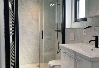 Moderne badeværelse med glasbrusekabine, toilet og hvid vask på De Parel ved Vakantiepark de Zeeuwse Parel.