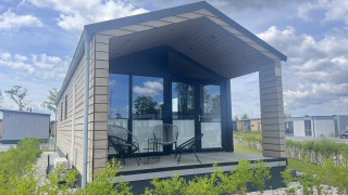 Eine moderne Lodge mit Glasfront und überdachter Terrasse bei De Parel, umgeben von Grün und Himmel.