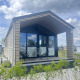 En moderne lodge med glasfacade og overdækket terrasse, set under en blå himmel ved De Parel.