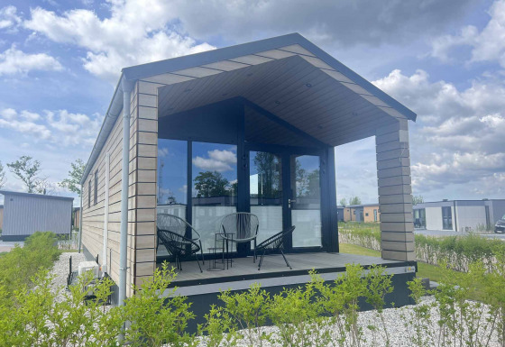 En moderne lodge med glasfacade og overdækket terrasse, set under en blå himmel ved De Parel.