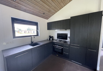 Cucina moderna con mobili scuri, fornello a gas e grande finestra in un lodge a De Parel, Paesi Bassi.