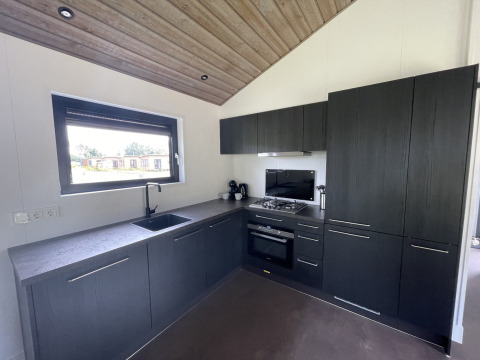 Moderne køkkenindretning med mørke skabe, gaskomfur og stort vindue i en lodge på De Parel, Nederlandene.