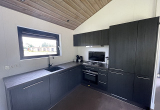 Moderne Küche mit dunklen Schränken, Gasherd und großem Fenster in einer Lodge bei De Parel, Niederlande.