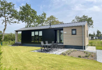 Moderne lodge ved De Parel i Vakantiepark de Zeeuwse Parel, Holland, med havemøbler og grøn plæne.