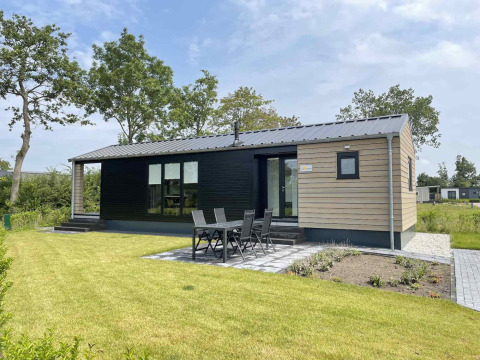 Moderne lodge ved De Parel i Vakantiepark de Zeeuwse Parel, Holland, med havemøbler og grøn plæne.