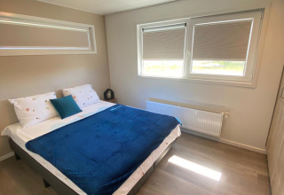 Dormitorio en la cabaña De Schelde del Vakantiepark de Zeeuwse Parel, Países Bajos, con cama y ventanas.