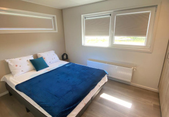 Dormitorio en la cabaña De Schelde del Vakantiepark de Zeeuwse Parel, Países Bajos, con cama y ventanas.