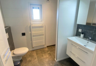 Salle de bain moderne avec WC, lavabo, miroir et porte-serviettes chauffant à Vakantiepark de Zeeuwse Parel.