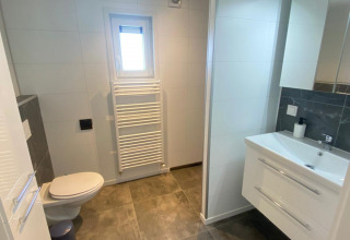 Moderne badkamer met wc, wasbak, spiegel en verwarmd handdoekenrek in Vakantiepark de Zeeuwse Parel.