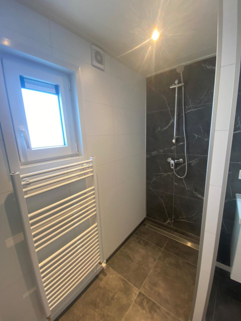 Salle de bain moderne avec douche, fenêtre, sèche-serviettes et carrelage sombre dans un lodge aux Pays-Bas.