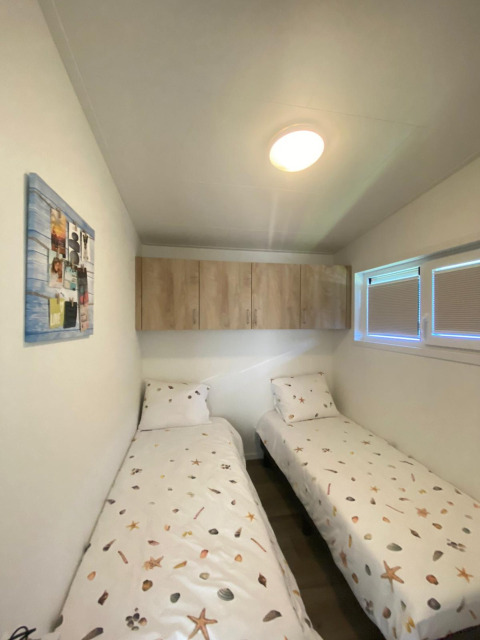Small room with two single beds with beach-themed covers, cabinets, and a window at De Schelde, Zeeuwse Parel.