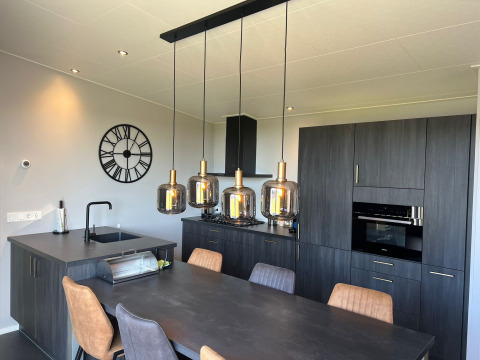 Moderne keuken met donkere kasten, eettafel, hanglampen en wandklok in lodge De Zeester, Nederland.