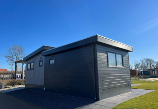 Die De Zeester Lodge im Vakantiepark de Zeeuwse Parel, Niederlande, bei sonnigem Wetter und blauem Himmel.