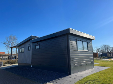 Die De Zeester Lodge im Vakantiepark de Zeeuwse Parel, Niederlande, bei sonnigem Wetter und blauem Himmel.