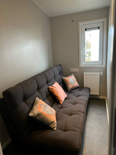 Gemütliches Zimmer mit schwarzem Sofa, bunten Kissen und Fenster in der Lodge De Zeester, Zeeuwse Parel, Niederlande.