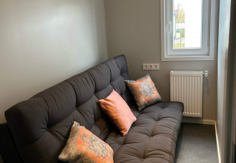 Gemütliches Zimmer mit schwarzem Sofa, bunten Kissen und Fenster in der Lodge De Zeester, Zeeuwse Parel, Niederlande.