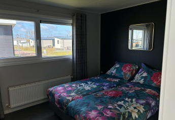 Bedroom with floral bedding at De Zeester, Vakantiepark de Zeeuwse Parel lodge in the Netherlands.
