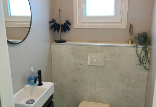 Modern toilet met wandcloset, kleine lavabo, ronde spiegel en raam bij lodge De Zeester, Nederland.
