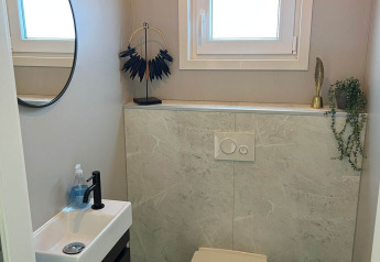 Moderne badeværelse med væghængt toilet, lille håndvask, rundt spejl og vindue i lodgen De Zeester, Nederlandene.