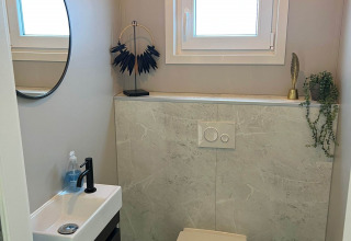 Salle de bain moderne avec toilettes suspendues, petit lavabo, miroir rond et fenêtre au lodge De Zeester, Pays-Bas.