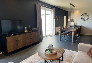 Sala y comedor modernos de lodge con pared negra, mesa, televisor y ventanas grandes en De Zeester, Países Bajos.