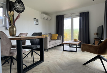 Modernes Wohnzimmer in der Lodge Dijkzicht im Vakantiepark de Zeeuwse Parel in den Niederlanden mit großen Fenstern.