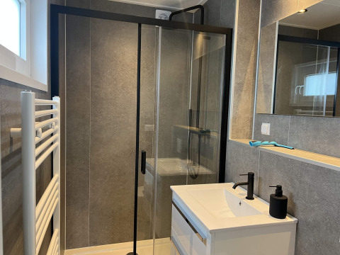 Bagno moderno con doccia in vetro, rubinetti neri e specchio nella lodge Dijkzicht al Vakantiepark de Zeeuwse Parel.