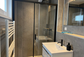 Baño moderno con ducha de cristal, grifería negra y espejo en la lodge Dijkzicht en Vakantiepark de Zeeuwse Parel.