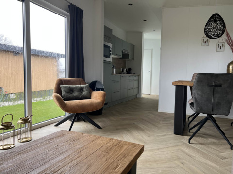 Interno di un lodge moderno con grandi finestre, poltrona e tavolo a Dijkzicht, Vakantiepark de Zeeuwse Parel.