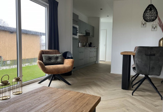 Interno di un lodge moderno con grandi finestre, poltrona e tavolo a Dijkzicht, Vakantiepark de Zeeuwse Parel.