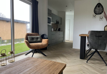 Intérieur de lodge moderne avec grandes fenêtres, fauteuil et table à Dijkzicht, Vakantiepark de Zeeuwse Parel.