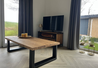 Modernes Wohnzimmer in der Dijkzicht-Lodge, Vakantiepark de Zeeuwse Parel, mit Holztisch und TV.