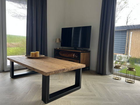 Modernes Wohnzimmer in der Dijkzicht-Lodge, Vakantiepark de Zeeuwse Parel, mit Holztisch und TV.