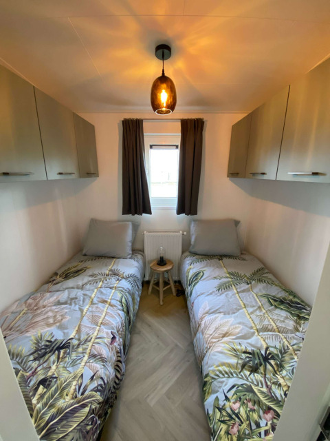 Cuarto pequeño con dos camas individuales, armarios modernos, ventana y ropa de cama de hojas tropicales.