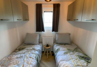 Cuarto pequeño con dos camas individuales, armarios modernos, ventana y ropa de cama de hojas tropicales.