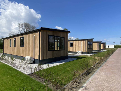 Holzhütten beim Noordzee Lodge unter blauem Himmel mit grünen Rasenflächen und Hecken.