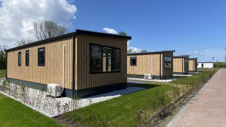 Lodge in legno al Noordzee lodge con cielo azzurro, prati verdi e siepi che circondano le strutture.