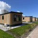 Trælodge hytter på Noordzee under en blå himmel med grønne græsplæner og hække foran bygningerne.