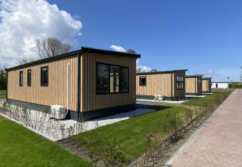 Houten lodges bij het Noordzee lodge, onder een blauwe lucht, met grasvelden en groene heggen eromheen.
