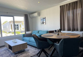 Moderne opholdsstue i lodge Noordzee, Vakantiepark de Zeeuwse Parel, Holland, med blå sofa og spisebord.