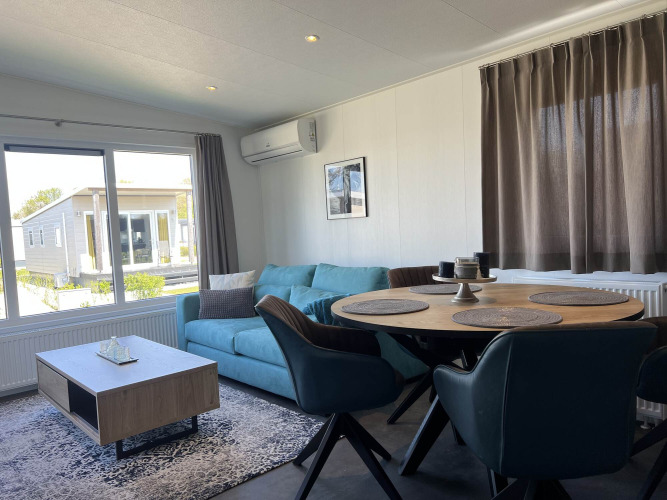Salón moderno en la cabaña Noordzee, Vakantiepark de Zeeuwse Parel, Países Bajos, con sofá azul y mesa.