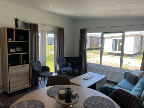 Moderne stue i en lodge ved Noordzee på Vakantiepark de Zeeuwse Parel, med lyse møbler og store vinduer.
