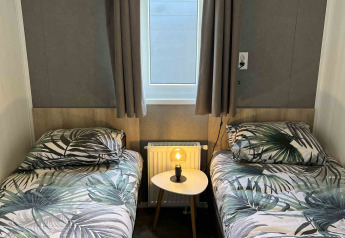 To enkeltsenge med tropiske dynebetræk, et lille bord med lampe og et vindue i en moderne lodge.