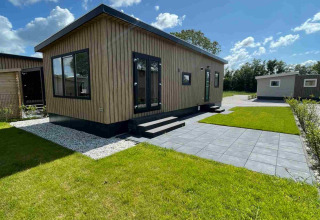 Een moderne houten lodge bij Vakantiepark de Zeeuwse Parel in Nederland met groen gras en terras.