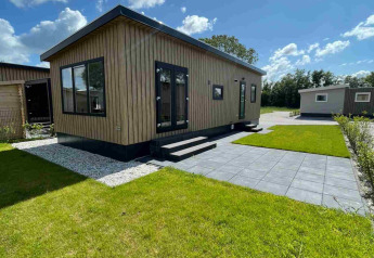 A modern wooden lodge at Vakantiepark de Zeeuwse Parel in the Netherlands with green lawn and patio.