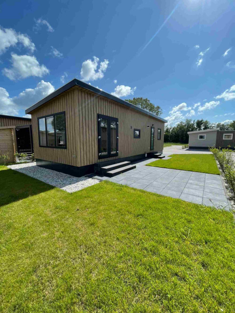 Et moderne træhuslodge på Vakantiepark de Zeeuwse Parel i Holland med grøn græsplæne og solskin.