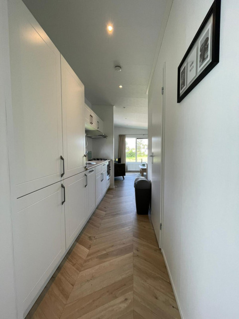 Modern hallway with chevron wood floor and white kitchen in a lodge at Vakantiepark de Zeeuwse Parel, Netherlands.