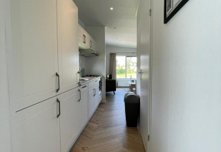 Moderne gang met houten vloer en witte keuken in een lodge op Vakantiepark de Zeeuwse Parel, Nederland.